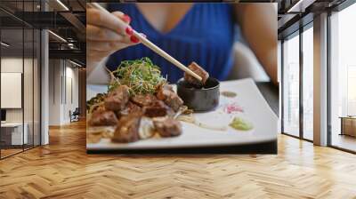 Young woman joyfully digs into her delicious gourmet beef meal, heartily using her chopsticks at a modern asian restaurant. she's enjoying her fresh japanese cuisine for an amazing lunch or dinner Wall mural