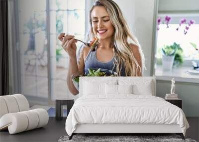 Young woman smiling confident eating salad at kitchen Wall mural