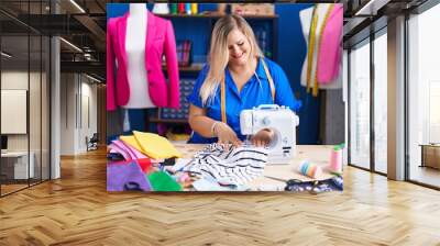 Young woman tailor smiling confident using sewing machine at sewing studio Wall mural