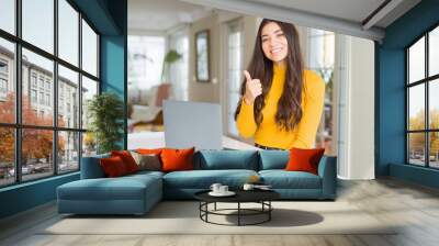 Young woman using computer laptop doing happy thumbs up gesture with hand. Approving expression looking at the camera with showing success. Wall mural