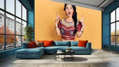 Young woman wearing bindi and bollywood clothing amazed and surprised looking up and pointing with fingers and raised arms. Wall mural