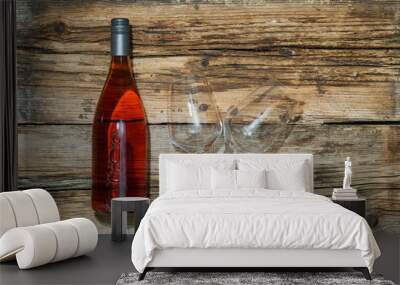 An unlabeled magnum rosé wine bottle with a dark gray metallic cap and two wine glasses are lying on a heavy weathered wooden board for individual mockup designs.  Wall mural