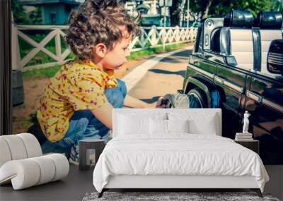 Young boy changing a tire on an black toy car. Children in the city amusement park Wall mural