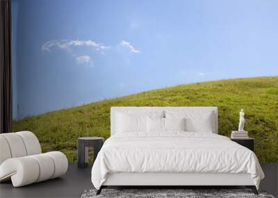 A green grassy hill with a single cloud in a bright blue sky. Wall mural