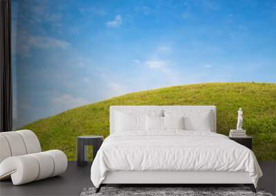 Lush green grass hill under a bright blue sky with scattered white clouds. Wall mural