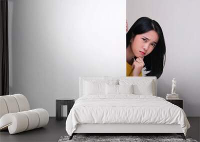 Young women peeking from behind wall with confused expression Wall mural