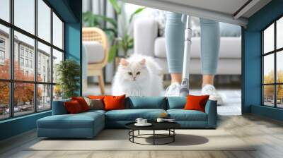 A person vacuums a carpet while a white cat watches, showcasing a clean home environment and pet-friendly cleaning. Wall mural