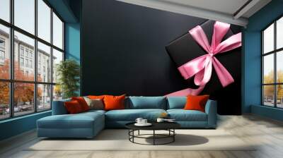 Black gift box with a pink ribbon on a black background Wall mural