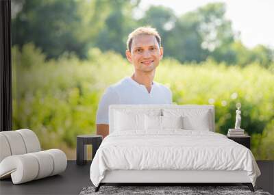 Bokeh green soft meadow background in nature park with portrait of smiling young happy man in summer in white shirt Wall mural