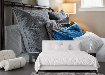 Closeup of decorative pillows cushions in shams and white bedding comforter duvet on bed in bedroom with illuminated lamp on nightstand and bright natural light from window Wall mural