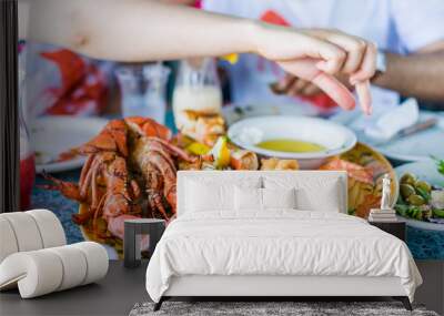 Closeup of lobsters and seafood on plate with hand reaching for garlic butter Wall mural