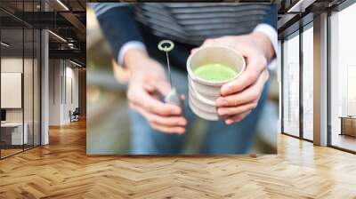 Man holding Japanese tea cup outside on backyard garden with whisk for matcha hot drink and foam Wall mural