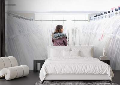 Young woman searching for wedding dress gowns in boutique discount store, many white garments hanging on rack hangers row Wall mural