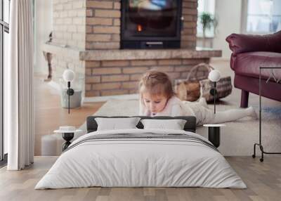 Beautiful little girl is reading a book by the fireplace. Cozy.Fall. Wall mural