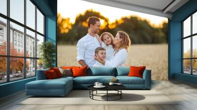 Beautiful young family at sunset in a wheat field. Happy parents with two children, a boy and a girl, in light clothes. Summer. Wall mural