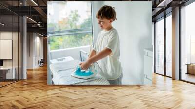 Cute 10 year old boy is doing homework and ironing clothes. Household appliances. Wall mural