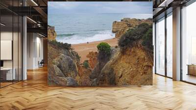 beautiful sandstone cliffs with view on two people standing on sand beach with sea waves and rock formation and blue sky background in Algarve Wall mural