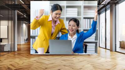 Businesswomen Celebrate Success: Two excited businesswomen celebrate a win on their laptop in a modern office environment, symbolizing teamwork, achievement, and the power of collaboration.  Wall mural