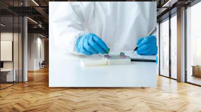 Doctor hand taking a blood sample tube from a rack with machines of analysis in the lab background, Technician holding blood tube test in the research laboratory. Wall mural