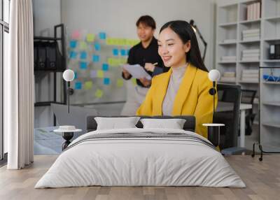 Focused Collaboration: Young businesswoman working on laptop in modern office with colleague in background  Wall mural