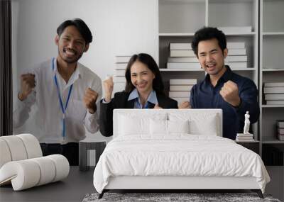 Office Triumph: A trio of ecstatic Asian professionals celebrate success in their modern office, fists pumping with joy. Wall mural