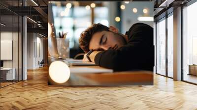 Exhausted Worker: A young man asleep at his desk, illuminated by warm lamplight, capturing the relatable struggles of late nights and overwork.  stress, tiredness, boredom Concept Wall mural