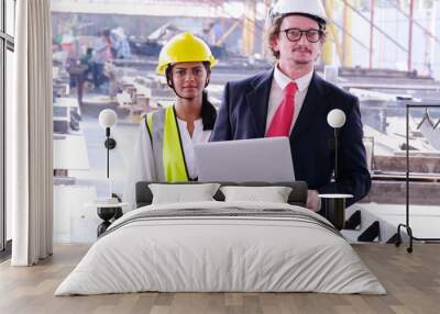 Engineer in safety helmet holding laptop working on job site. Wall mural