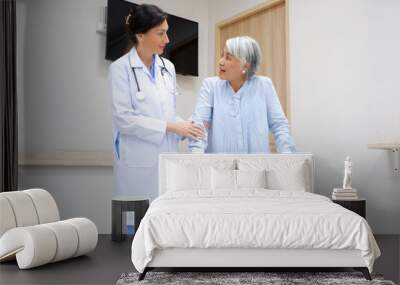 Female doctor supporting an elderly female patient holding a cane. Wall mural