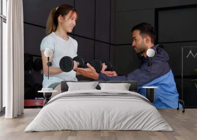 Young woman and trainer exercising with dumbbells in a fitness gym. Wall mural