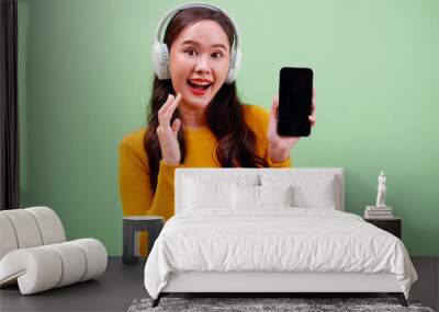 Young woman smiling with headphones and using smartphone. Wall mural