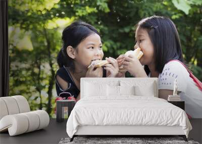 Two girls eat happy and fun sandwiches in the garden, And next to green vegetable and red alarm clock. Small party on holiday Wall mural