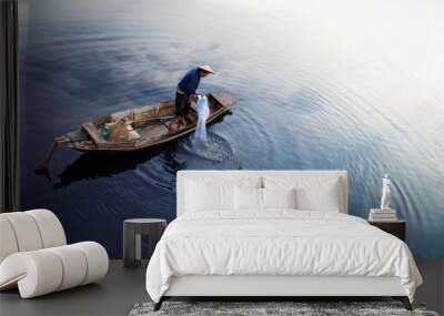 Asian fisherman on wooden boat casting a net for catching freshwater fish in nature river in the early morning before sunrise Wall mural