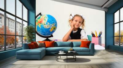 A little schoolgirl sits at her desk, draws, writes, looks at the globe and does her geography homework. isolate. Wall mural