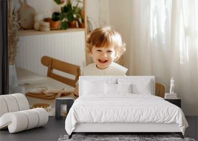 little boy 2 years old sits and laughs in the kitchen at the table on a bright day
 Wall mural