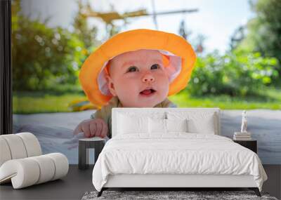 A cheerful kid little baby in a funny yellow panama lies on his tummy in nature on the grass Wall mural