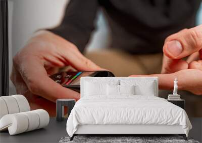 A man at home uses a glucose meter to measure blood glucose. Piercing a finger with a needle Wall mural