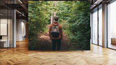 A young blond man with a backpack walks in the woods on a path, a photo from the back Wall mural