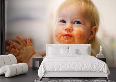 Cute toddler little child eats in a bib on a high chair, mouth dirty in sauce Wall mural