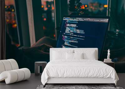 The code is on a laptop on a wooden table in front of the window  in the dark with a view of the lights of the night city, color lighting in the room, home decor	 Wall mural