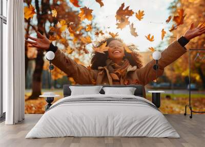 Casual joyful woman having fun throwing leaves in autumn at city park Wall mural