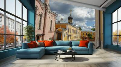 Church courtyard with brightly colored two story stone buildings and black domes in the background with the rays of the bright sun on the blue sky Wall mural