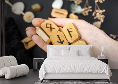 Stack of wooden runes in hand on black table background. Scandinavian magical esoteric symbols and signs for divination and prediction of the future and destiny, esotericism concept. Wall mural