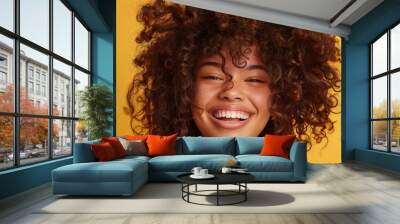 Delighted girl with curly hair laughing joyfully, dressed in a vibrant coral jacket. Wall mural