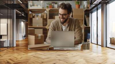 Young entrepreneur working on a laptop in a stylish home office, surrounded by packaging boxes and plants, focused on online business. Wall mural