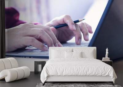 Hands of a man in red sweater holding a pencil while typing on laptop computer notebook keyboard in the office. Closeup with left and top copy space. Cropped as a banner or web strip. Wall mural