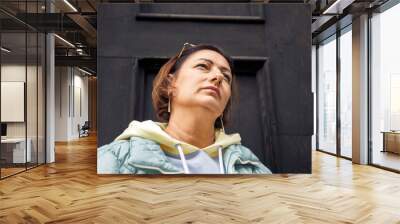 Confident woman in casual attire standing against a dark wooden door Wall mural