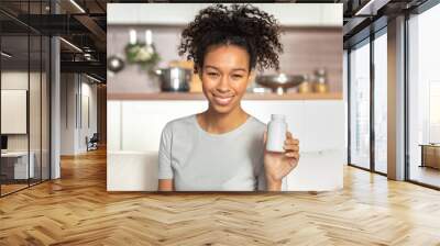 Happy young African American woman holding bottle of dietary supplements or vitamins in her hands. Close up. Healthy lifestyle concept Wall mural