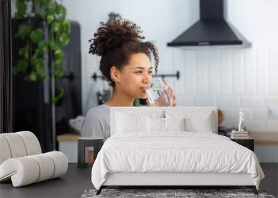 Healthy lifestyle concept. Beautiful young Afro American woman drinking clean water standing at home in the kitchen, copy space Wall mural