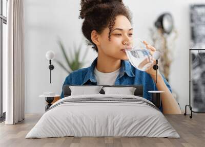 Healthy lifestyle concept. Happy African American woman entrepreneur or employee drinking clean water sitting in the office Wall mural