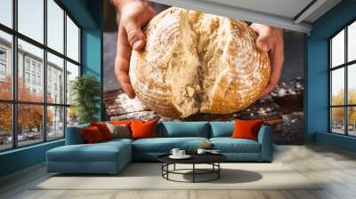 Male baker breaks freshly baked loaf of bread Wall mural